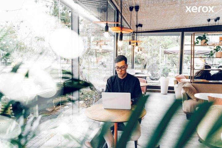 Un homme travaille avec diligence sur son ordinateur portable dans un café animé, immergé dans ses tâches au milieu d'un environnement animé.