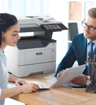 Un homme et une femme assis à une table, engagés dans une conversation tandis qu'une imprimante Xerox® est positionnée à proximité.