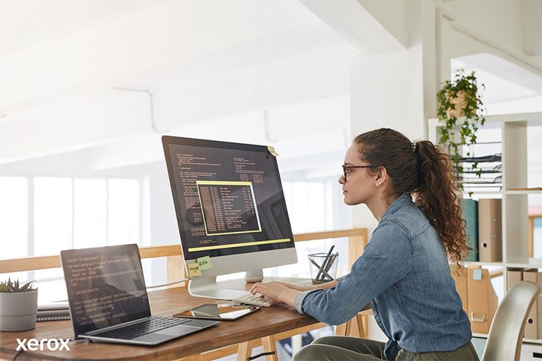 Une femme à son bureau, occupée avec un ordinateur et un ordinateur portable, démontrant sa productivité dans un espace de travail moderne.